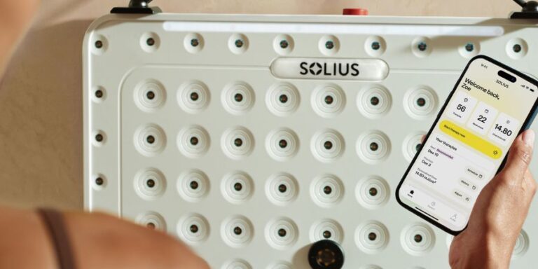 Solius UVB light therapy device mounted on wall with app showing personalized dosing on phone screen